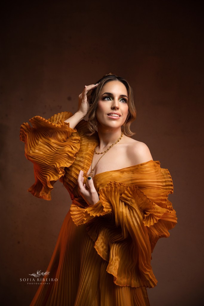 a smiling portrait captured in a gold pleated gown against a taupe backdrop