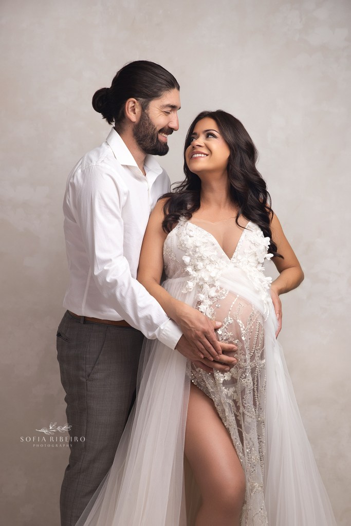 mom and dad to be share a sweet smile together while cradling baby bump during a maternity photography session in nj