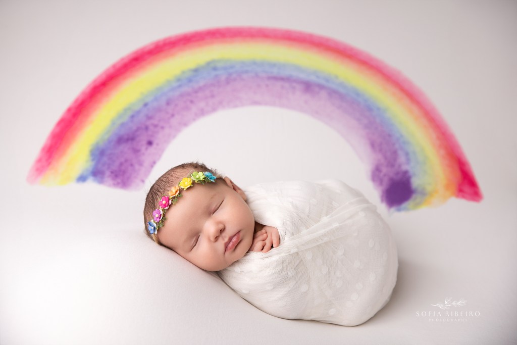 nj newborn photographer captures an odd to this rainbow baby with a tiny rainbow headband and backdrop, in budd lake nj