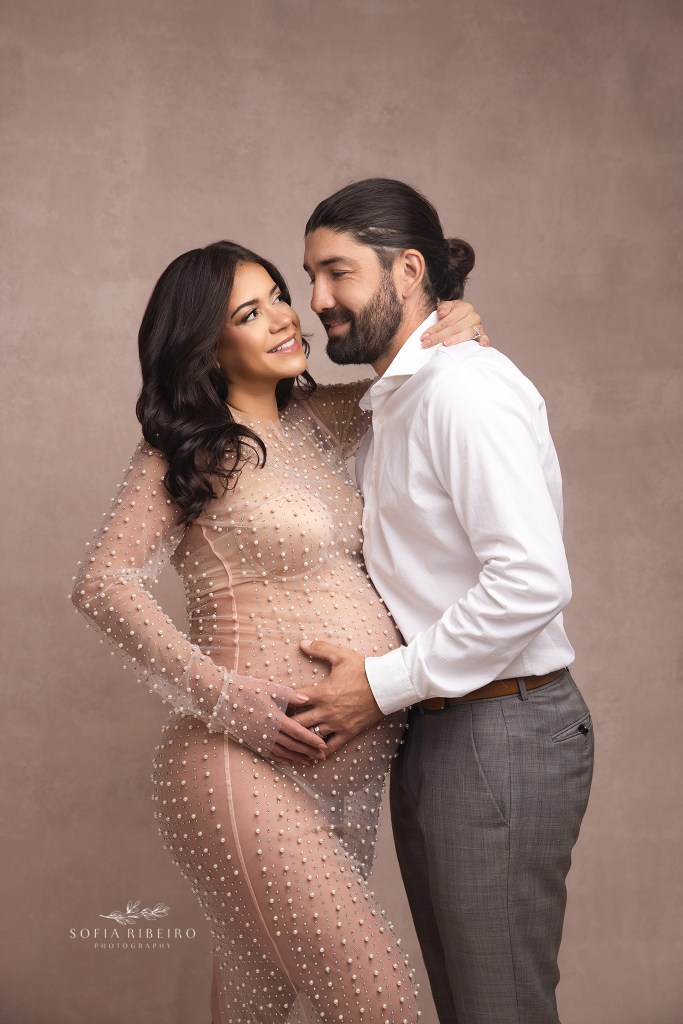 parents to be cradle the baby bump against a pink backdrop in a nj maternity photography studio