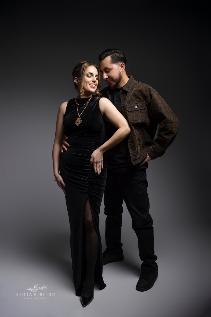 an intimate couples pose in shades of black against a dark grey backdrop