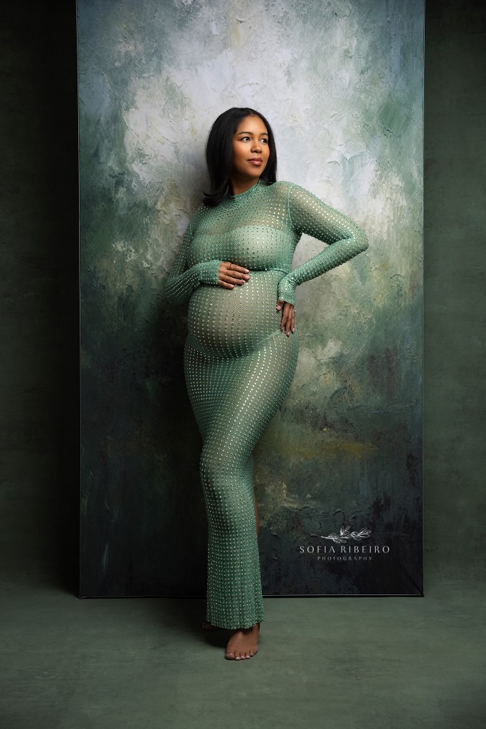 nj maternity photographer captures luxury, fine art portraits for expectant mothers. Mom poses in a glittering green jeweled gown against a painted green backdrop highlighting the baby bump