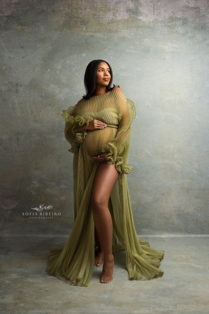 mom strikes a powerful pose in a green pleated high end maternity gown against a green painterly backdrop in nj