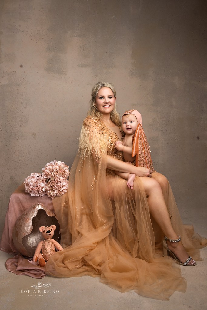 mom poses, mother of dragons style in nudes and golds, with baby dragon wings on her youngest child for a mother daughter photo shoot in nj