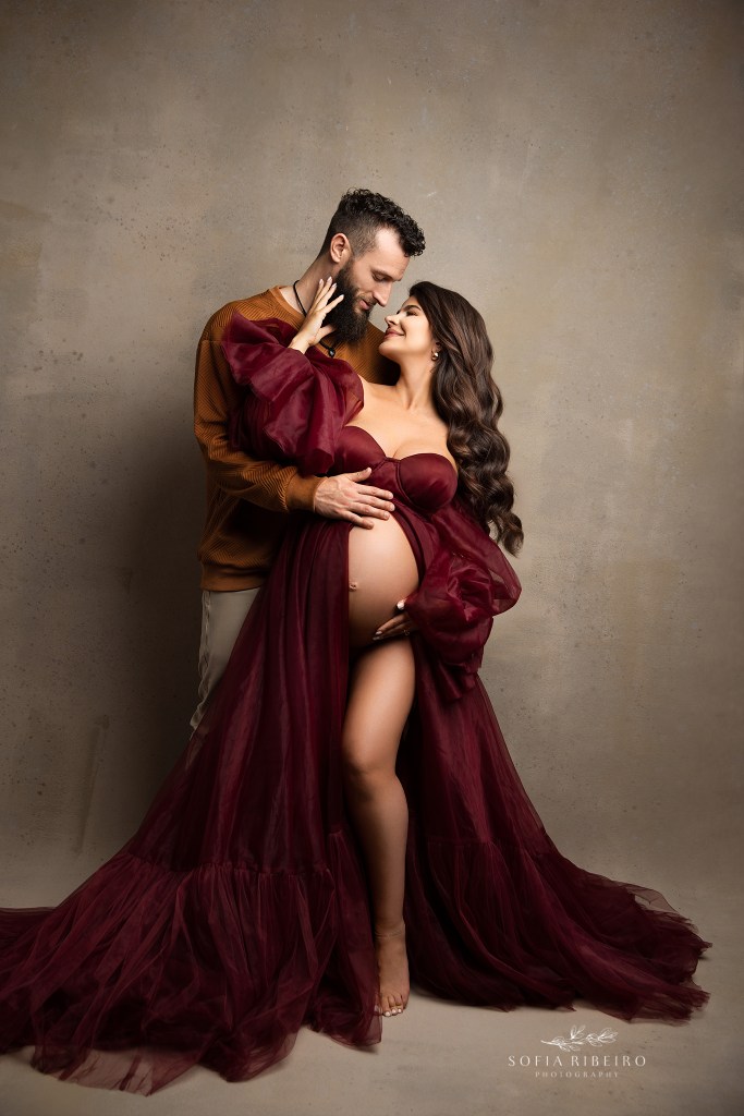 mom and dad share a sweet smiling moment together in autumnal shades against a taupe backdrop