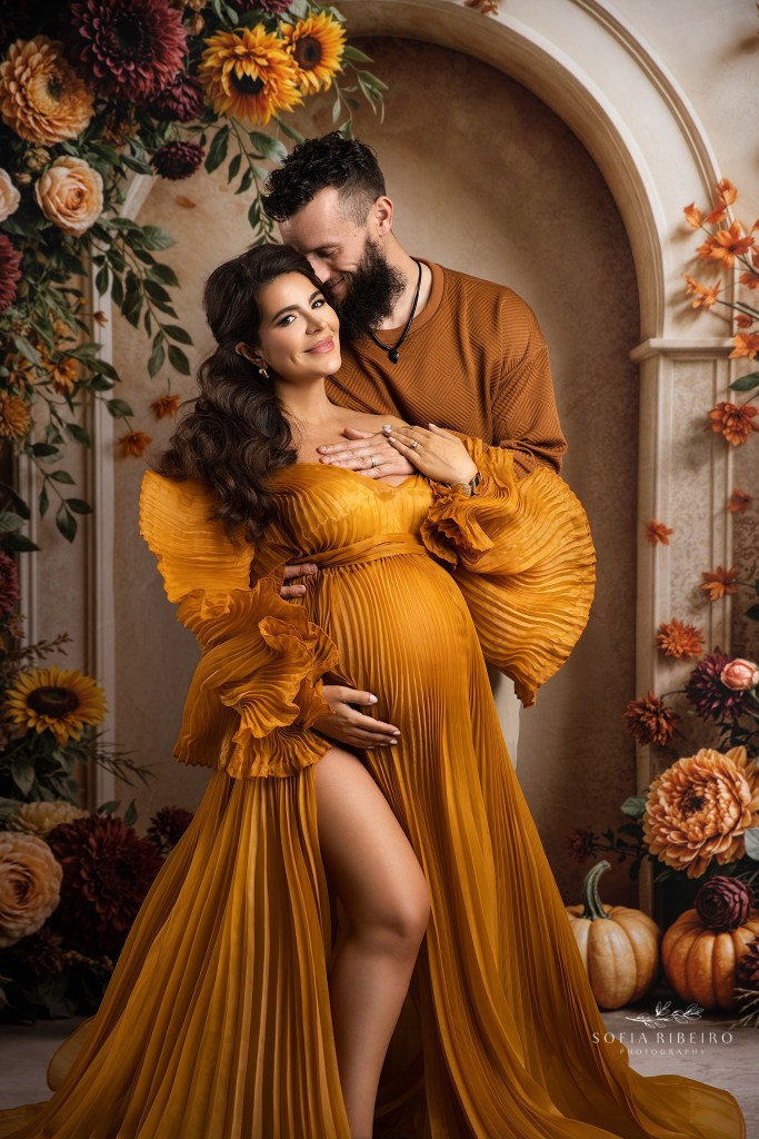 a tender moment between mom and dad, proudly showcasing the baby bump in a pleated mustard gown