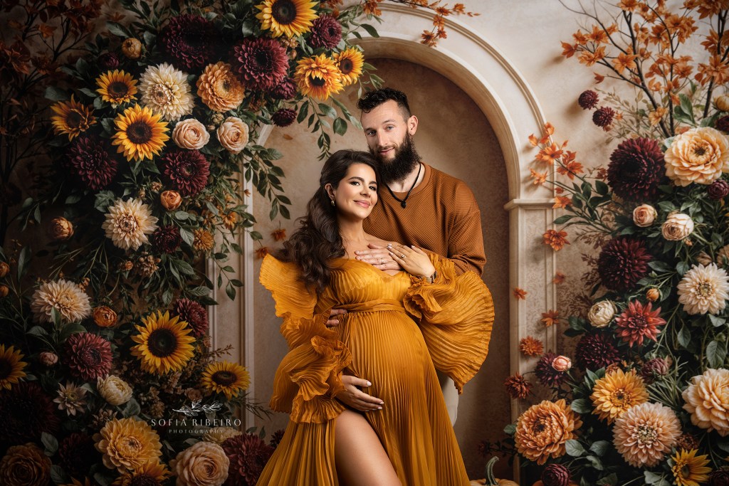 a tender moment between mom and dad, proudly showcasing the baby bump in a pleated mustard gown