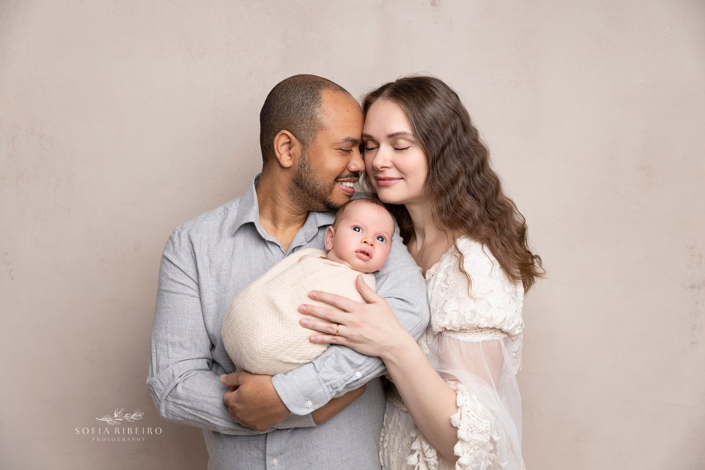 new parents snuggle together with a newborn baby boy during a photo session in a newborn photographer's studio in nj
