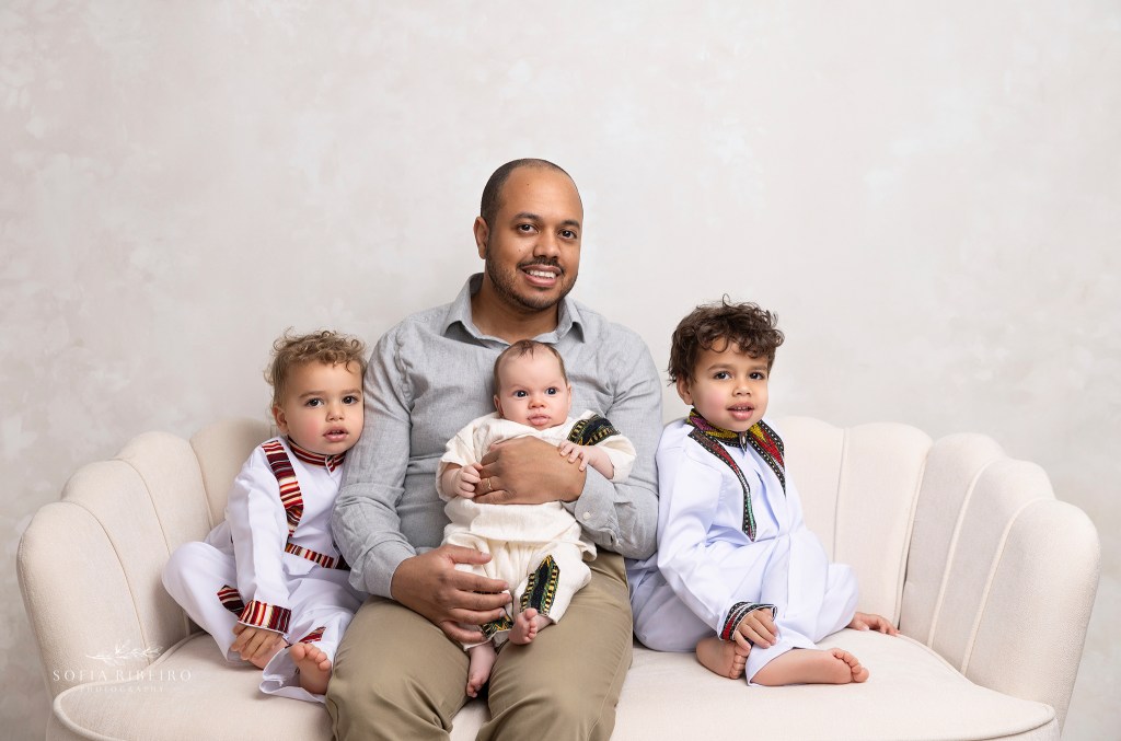 dad poses with his three baby boys during a newborn session in traditional clothing