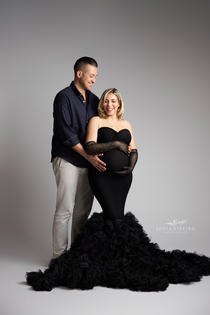 mom and dad share a sweet moment, laughing while cradling the baby bump in a black ensemble