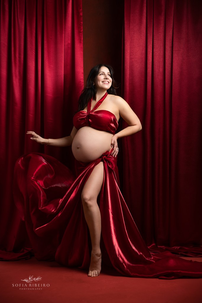 a smiling mom draped in red flashes her baby bump