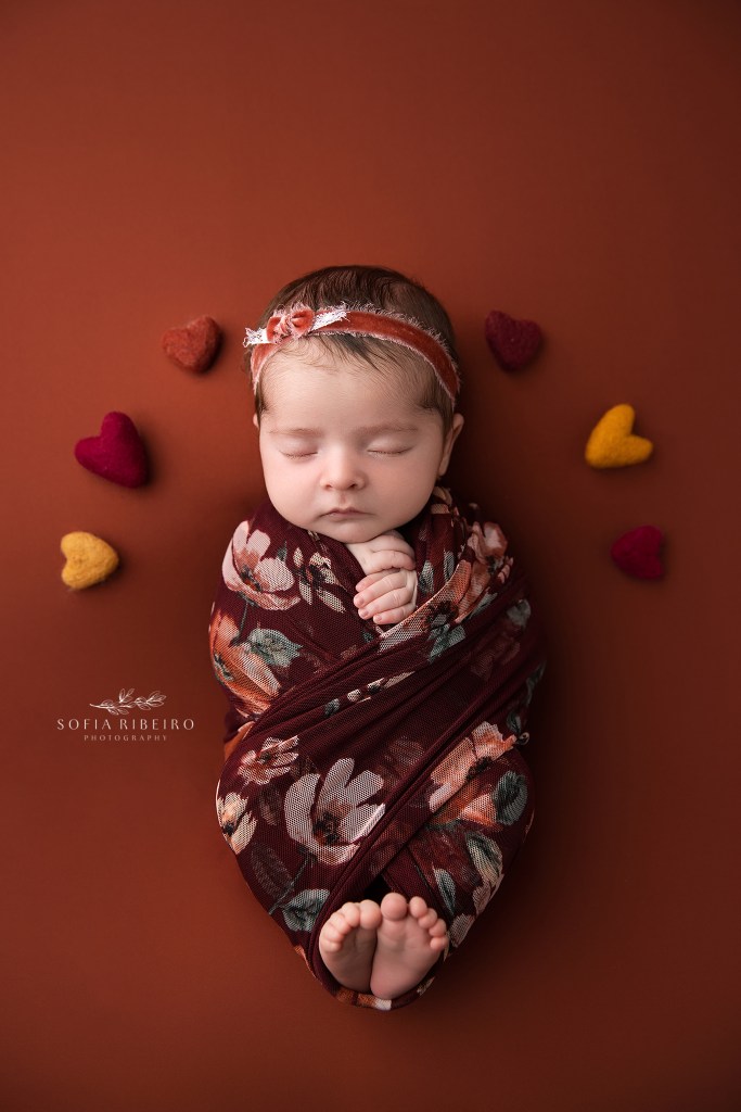 baby is wrapped in a fall floral with orange backdrop in nj newborn photographer's studio