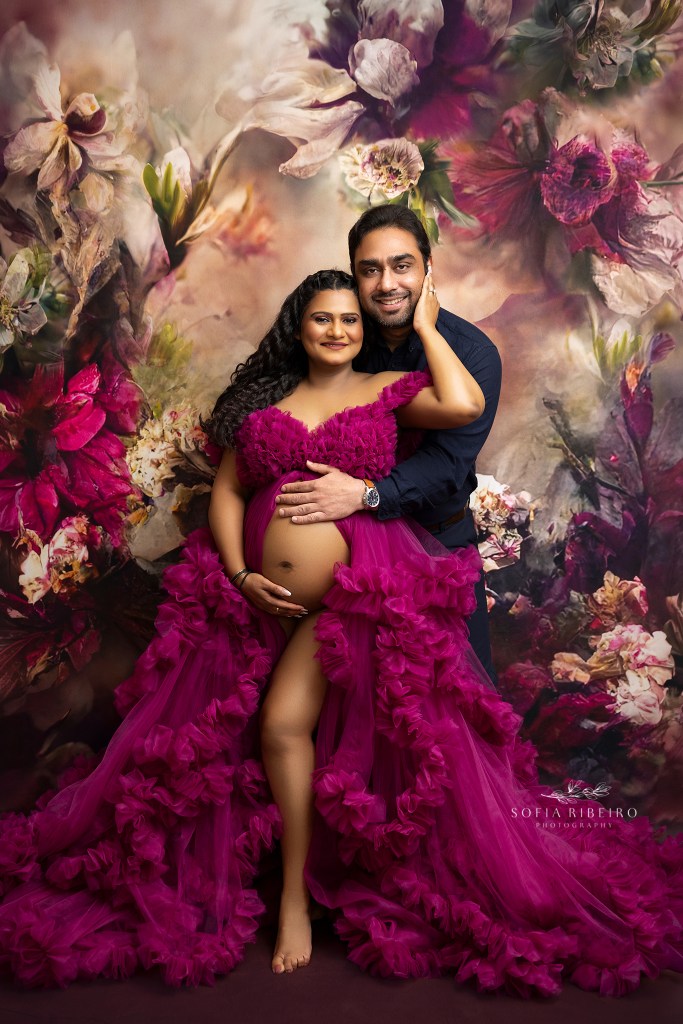 a pink floral bakcdrop frames mom and dad to be in a bold pink ruffled gown