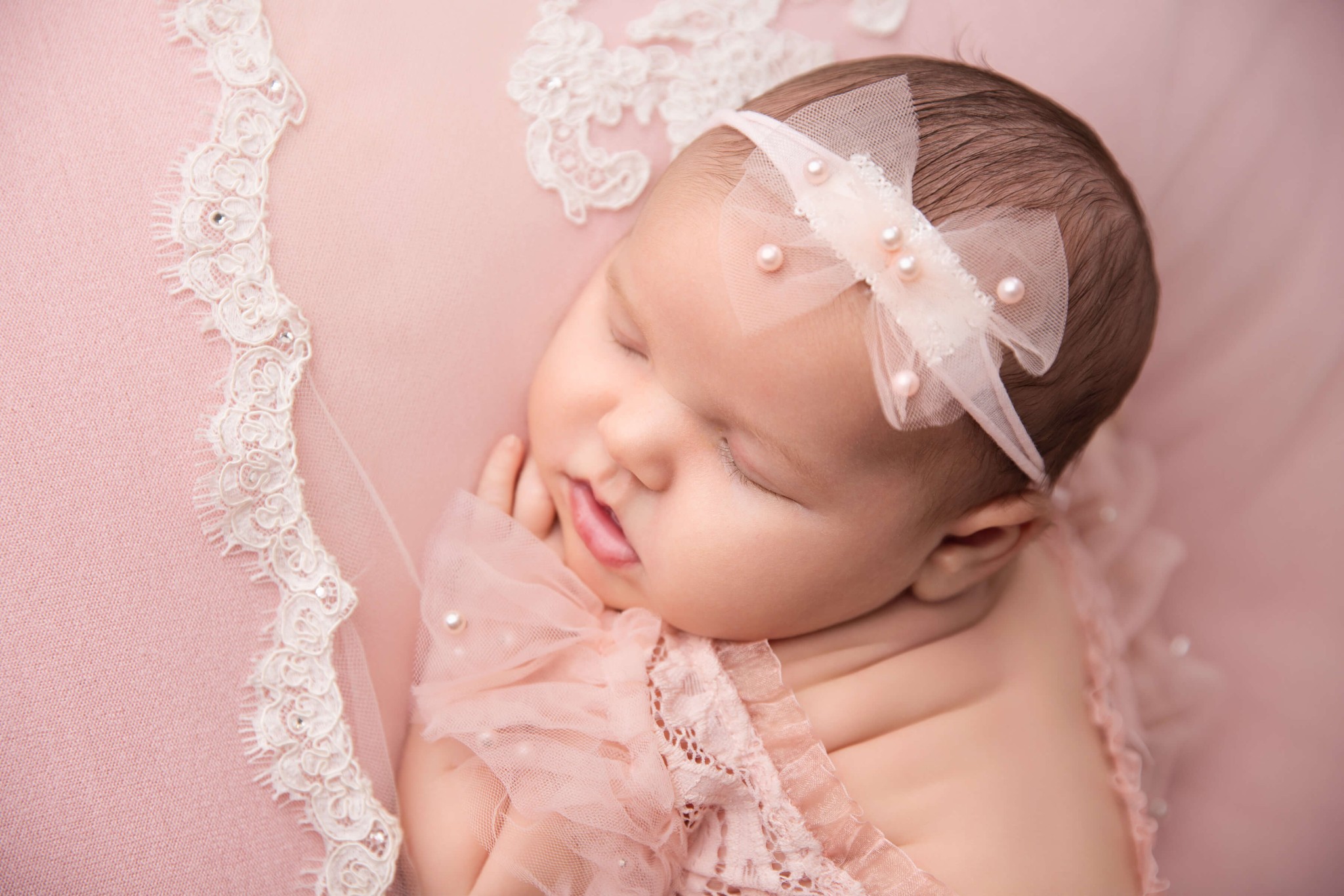 a look down at a sleeping newborn girl on a pink bed in a matching onesie and headband thanks to baby sleep consultants in nj