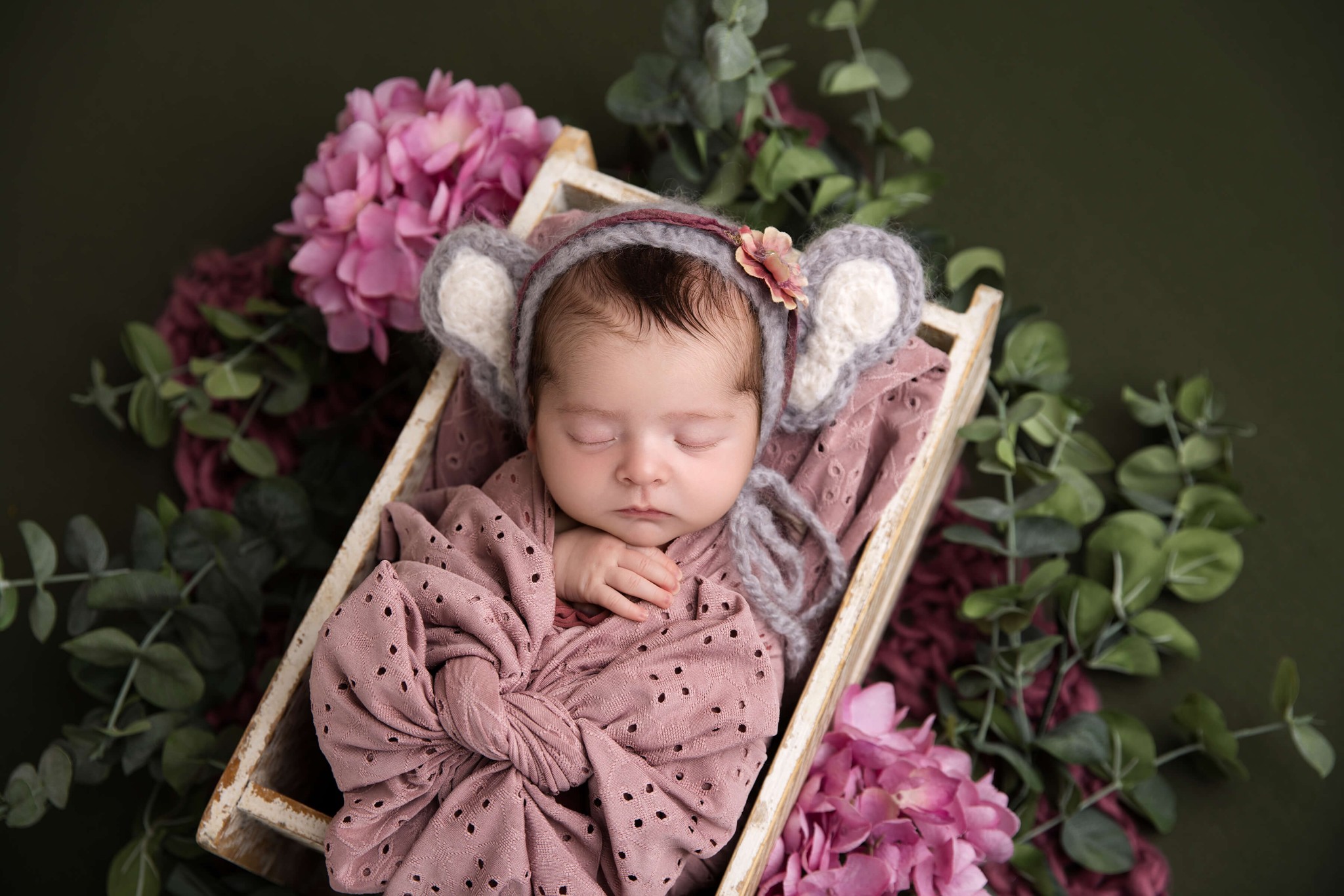 A newborn baby sleeps in a pink swaddle in an apple box with grey bonnet with ears after visiting daycares in morristown, NJ