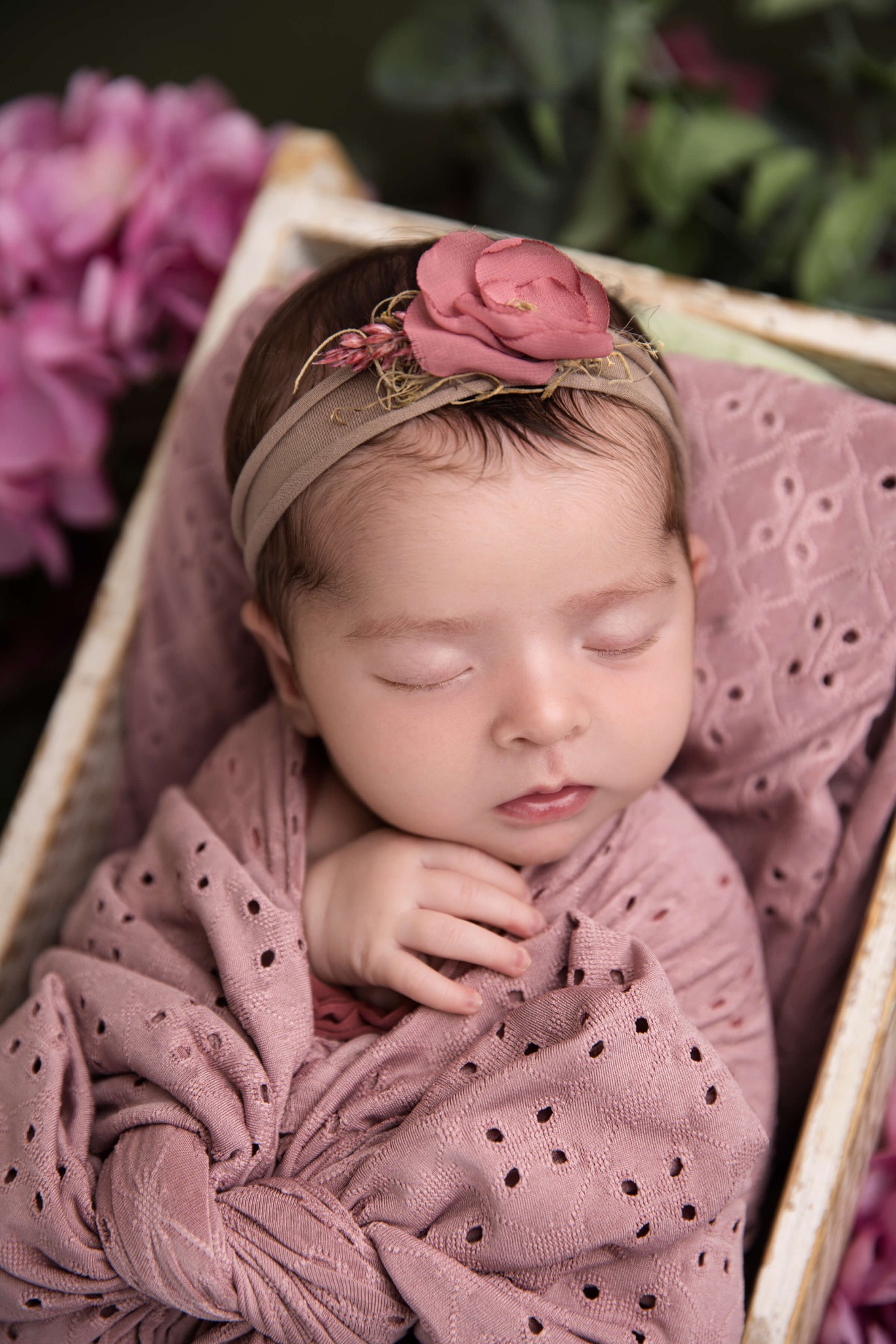 A sleeping newborn baby in a pink swaddle in a wooden box in a garden after visiting daycares in morristown, NJ