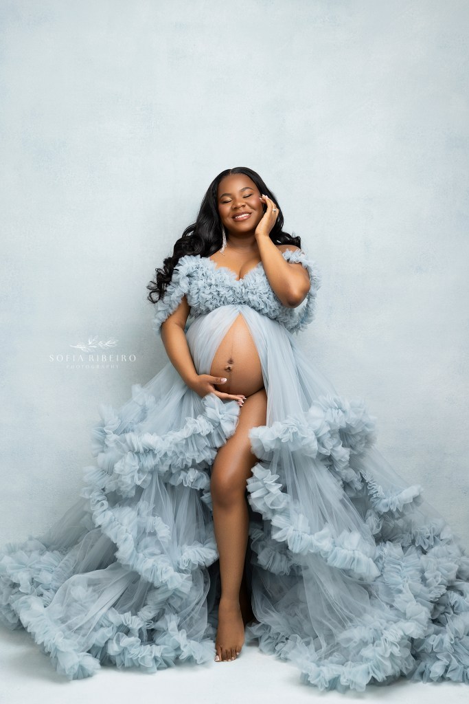mom to be in blue tulle with baby bump exposed and jeweled earrings against a blue backdrop