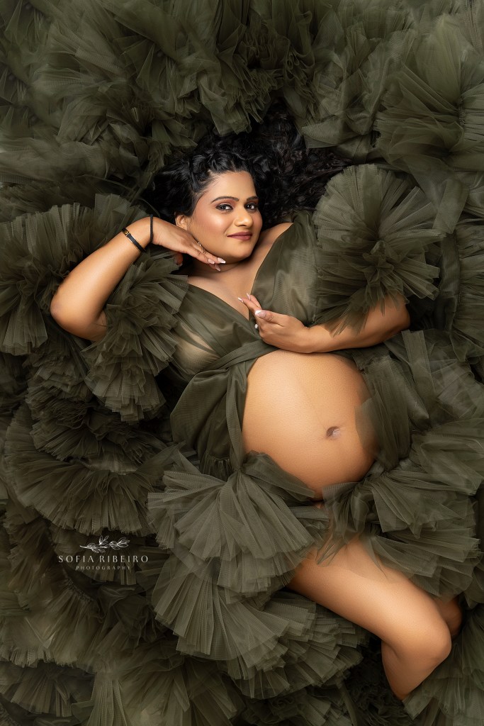 elegant hands frame mom in a lie down shot in green tulle, exposing her baby bump