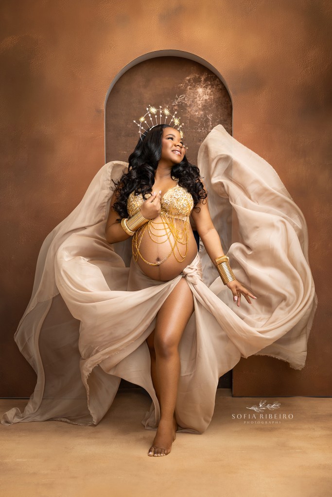 mom is the essence of a regal goddess in flowing fabric and gold halos during her maternity portraits in nj
