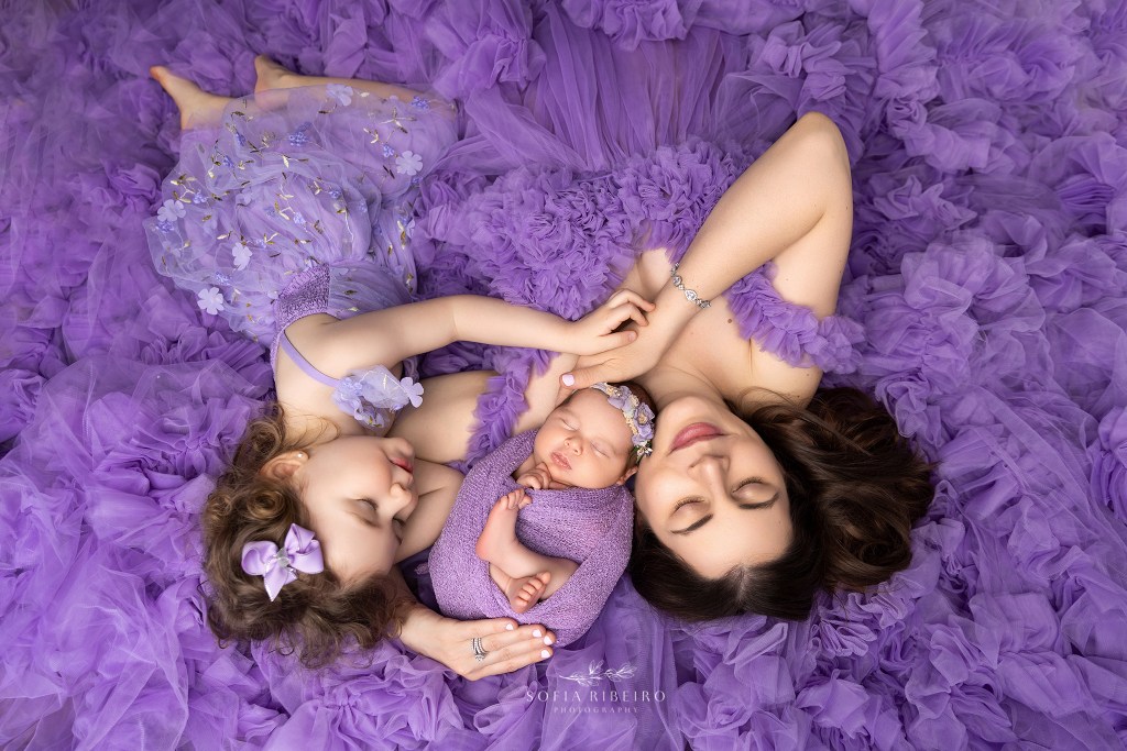 a lie down photo in purple tulle of mom, baby, and big sister