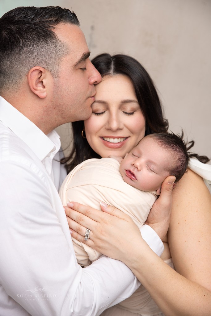 a closeup of mom and dad pose together lovingly with baby number three