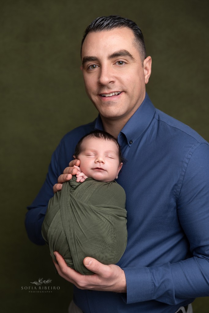 dad holds his new baby close for a newborn photo, both smiling