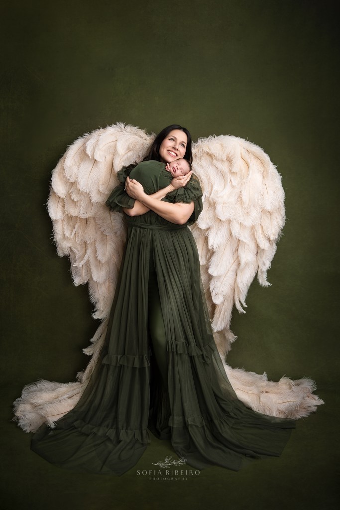 the third baby in their family is cradled by mom wearing angel wings
