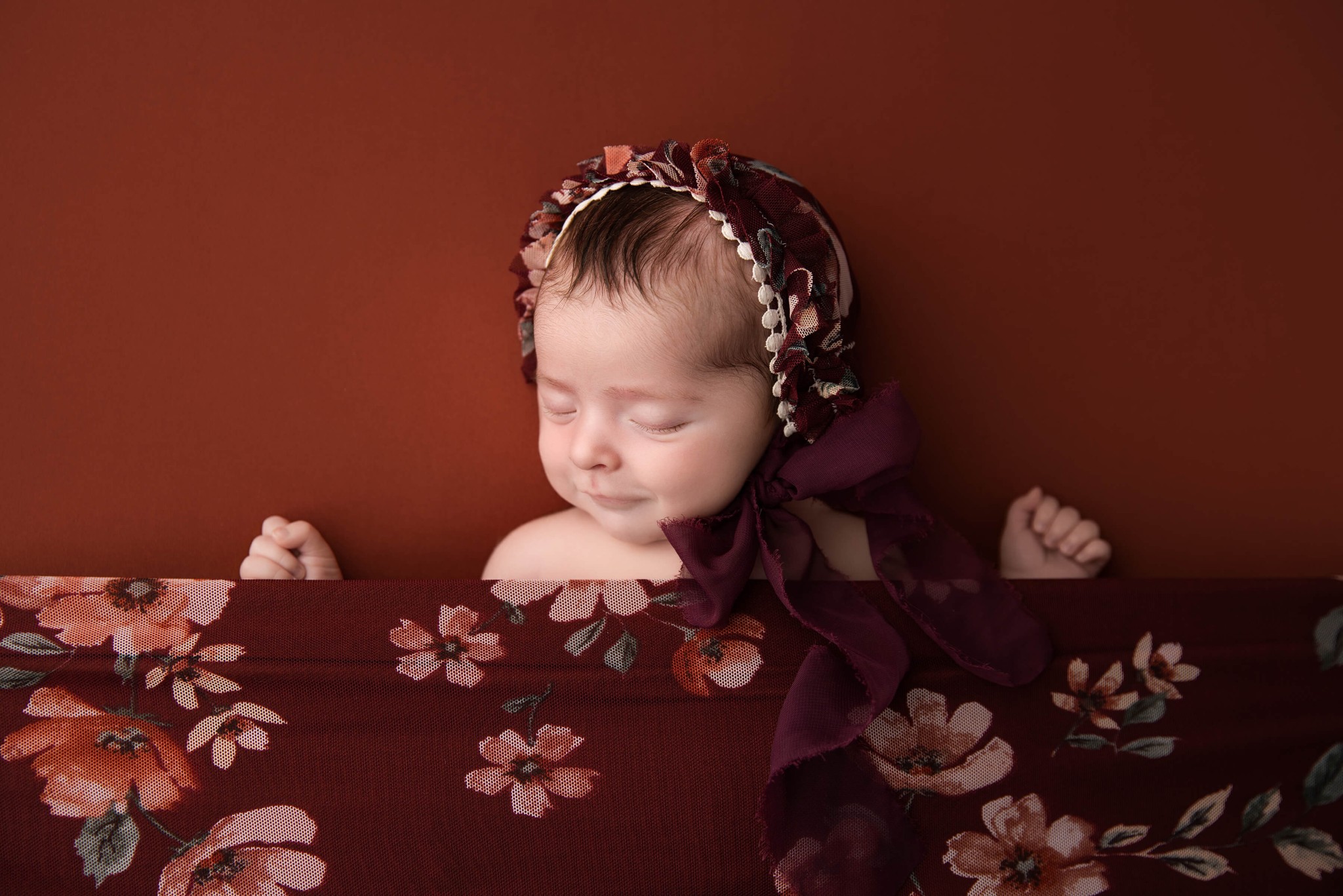 A sleeping newborn with arms spread under a flower print blanket