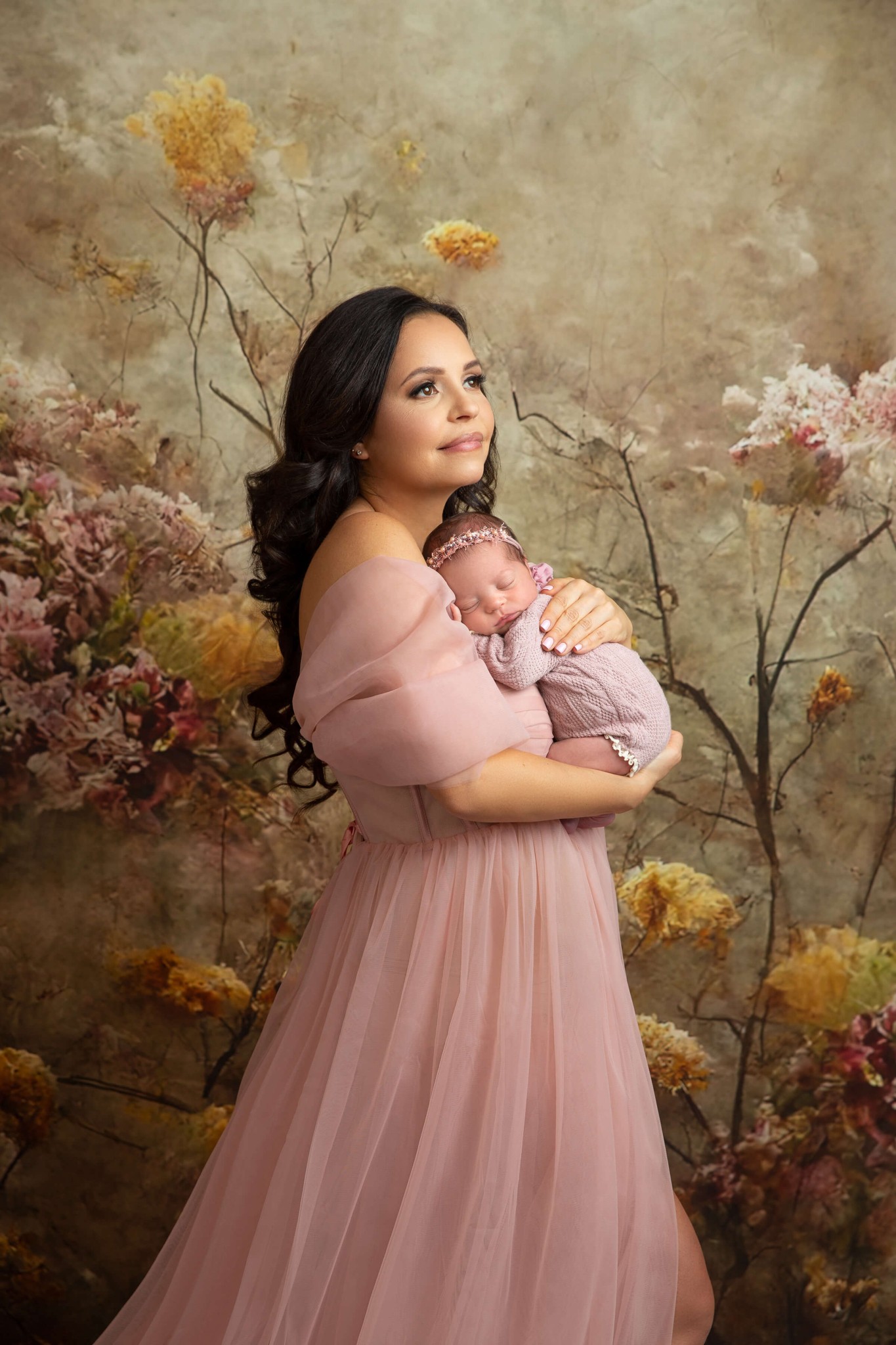 A new mom stands smiling cradling her newborn daughter against her chest in a pink dress after finding pediatricians in Millburn, NJ