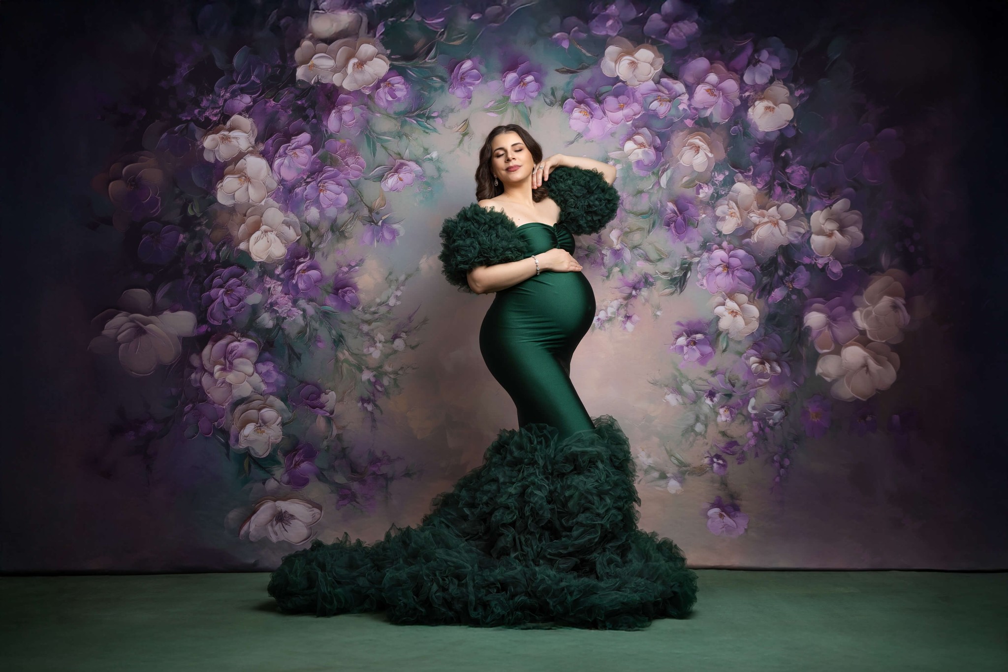 A mom to be stands in a glamorous green maternity gown in a studio