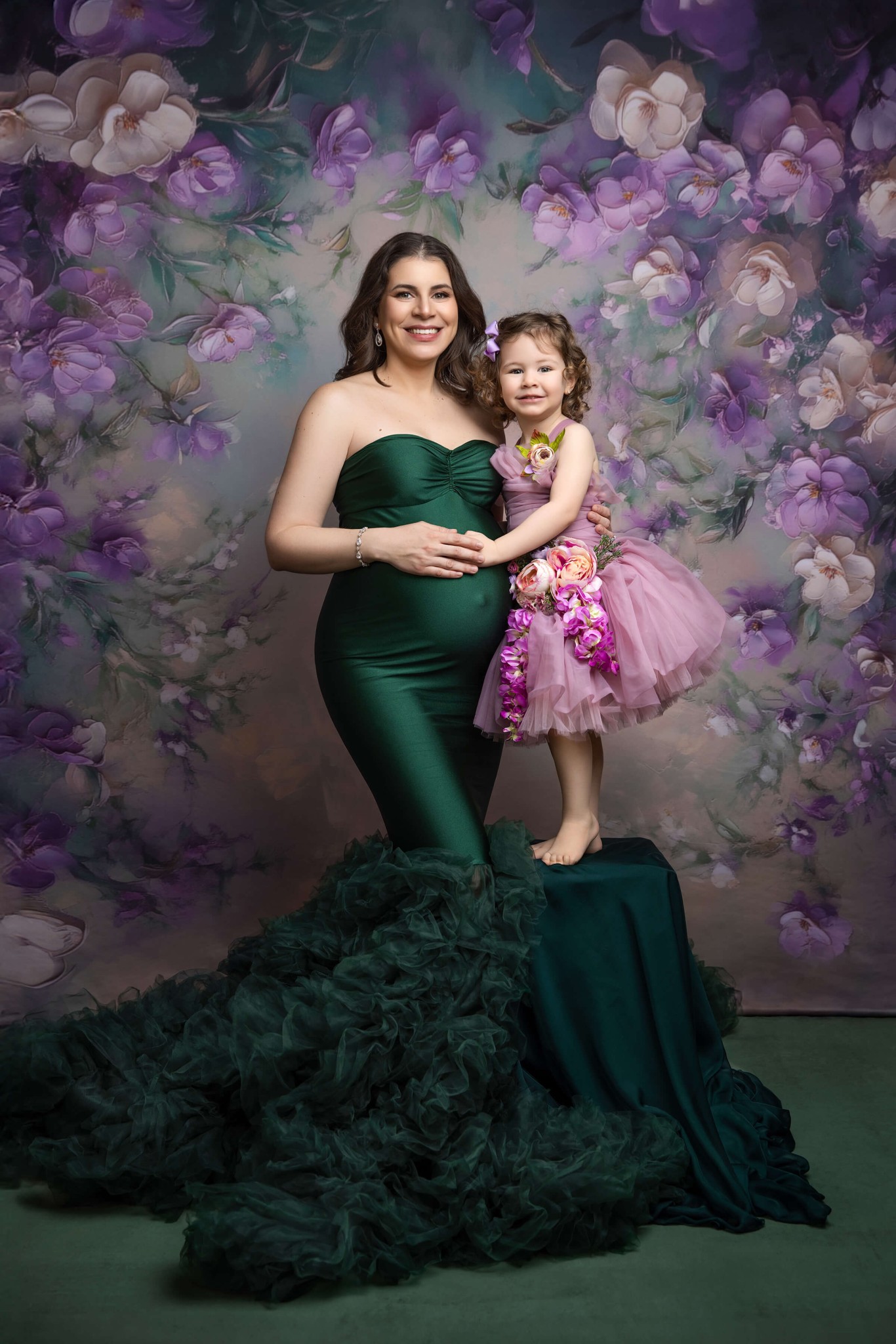A pregnant woman rests a hand on the bump while standing in a studio with her toddler daughter in a purple dress after some prenatal yoga in north jersey