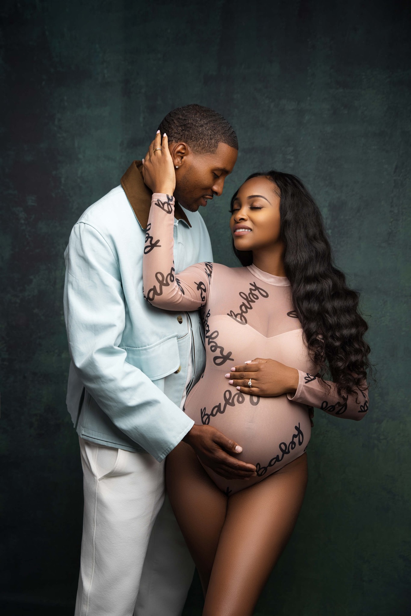 A woman in a bodysuit snuggles with her partner in a blue jacket in a studio after enjoying prenatal yoga in union county nj