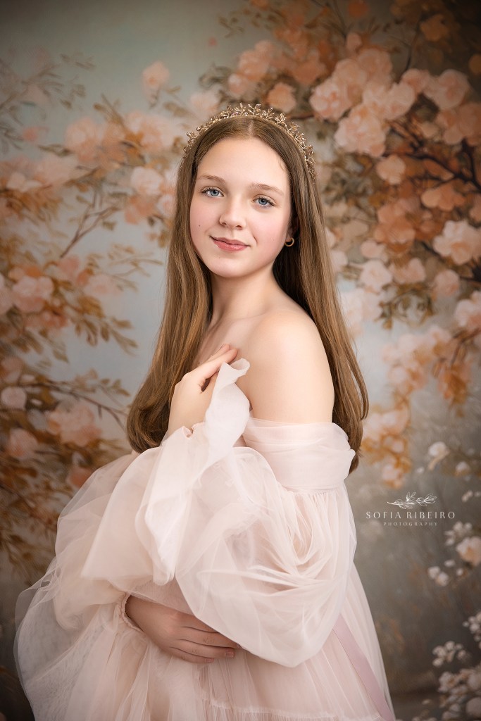 a closeup bridgerton type portrait against a floral backdrop of a young girl in soft pink tulle