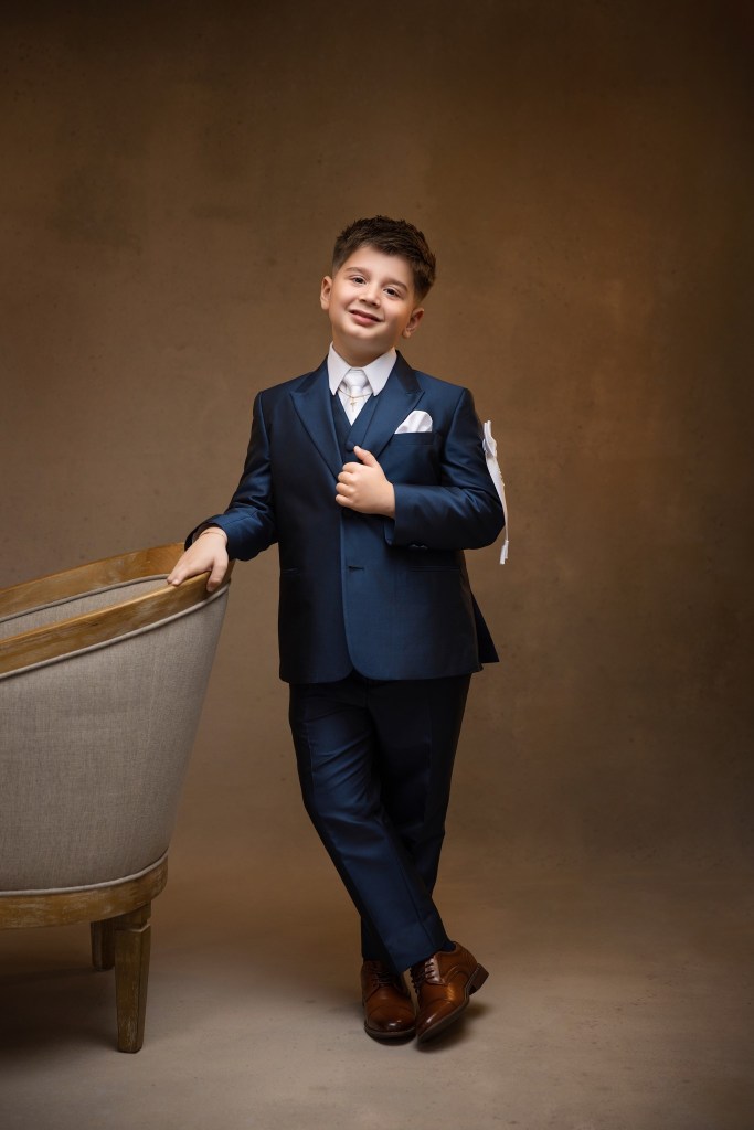 nj communion photographer poses boy against an upholstered chair