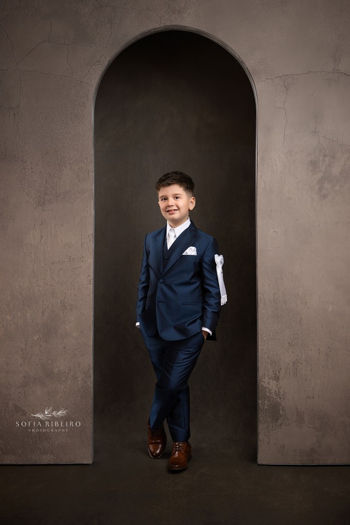 communion portrait boy in a navy suit against a brown backdrop