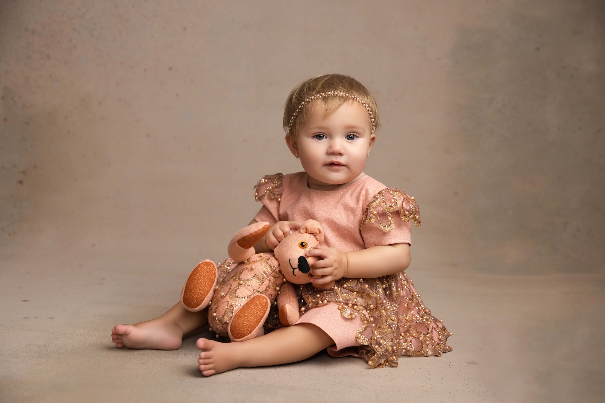 A toddler girl in a pink dress sits in a studio playing with a stuffed bear after visiting pediatric dentists in Morristown, NJ