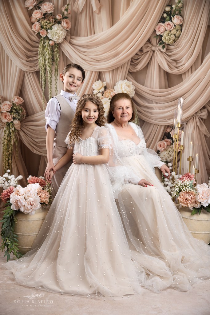 a portrait of grandmother and her grandkids agaqinst a draped beige and floral backdrop for mother's dazy