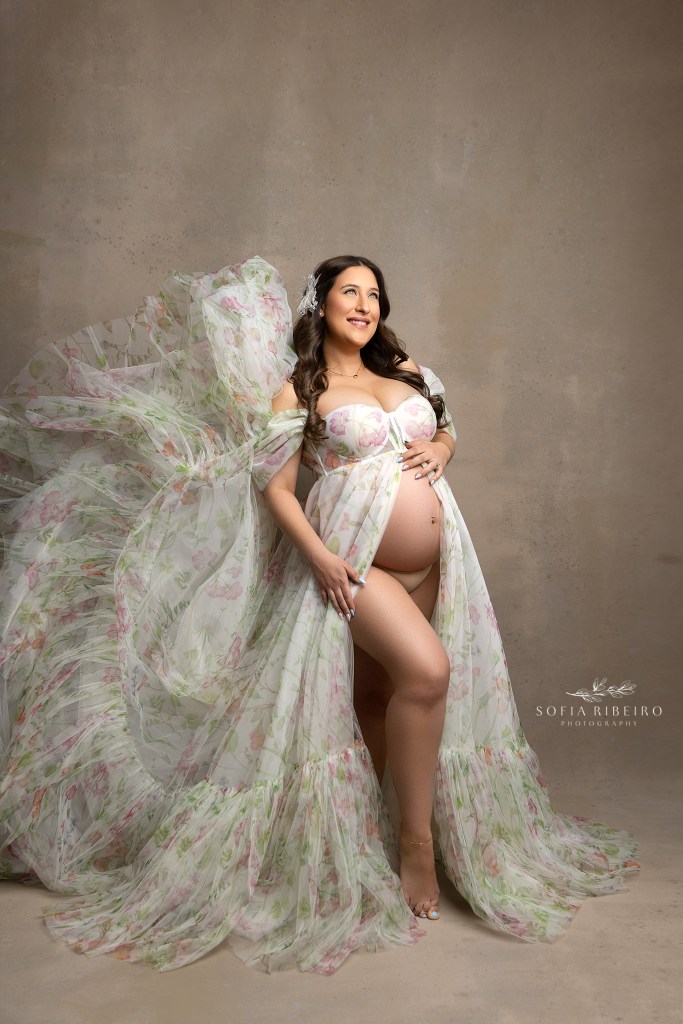 mom to be smiles while cradling her baby bump in an ethereal flowery gown shot by an nj maternity photographer