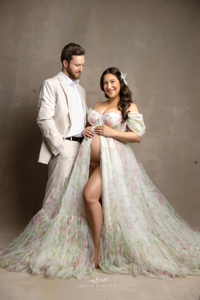 mom and dad share a sweet portrait together with baby bump exposed in a put together look of suiting and soft floral gown