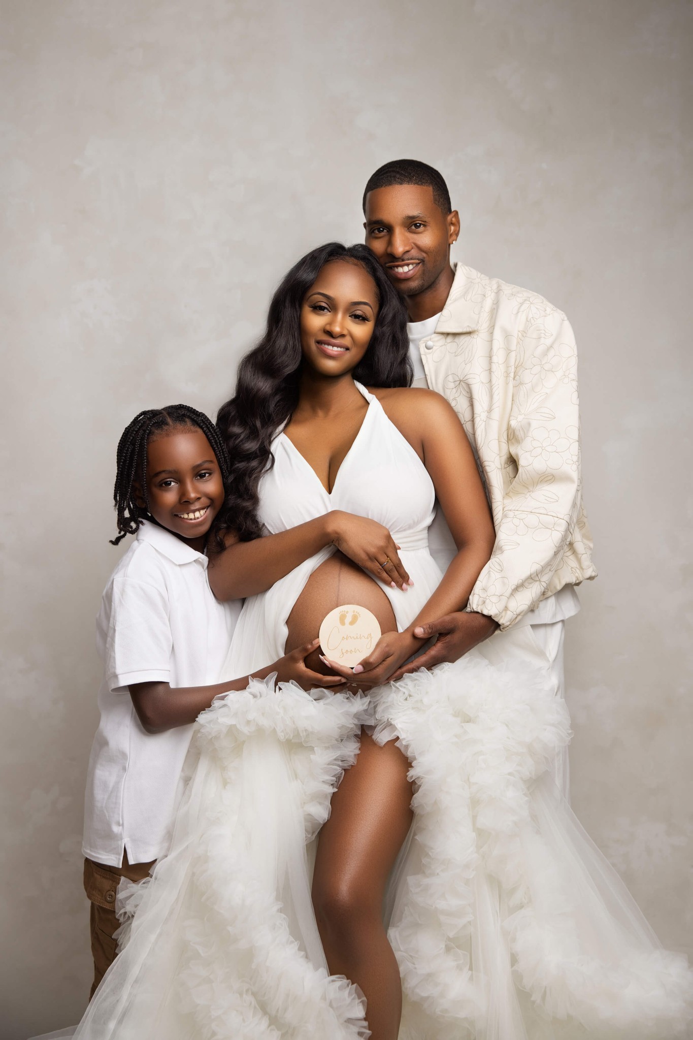Happy mom and dad hold a coming soon sign on mom's pregnant bump with their young son in a studio