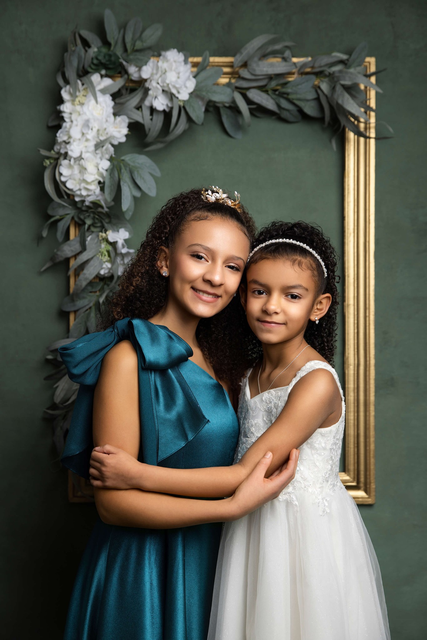 Smiling young sisters hug in white and teal gowns in a studio after meeting pediatricians in bergen county, nj