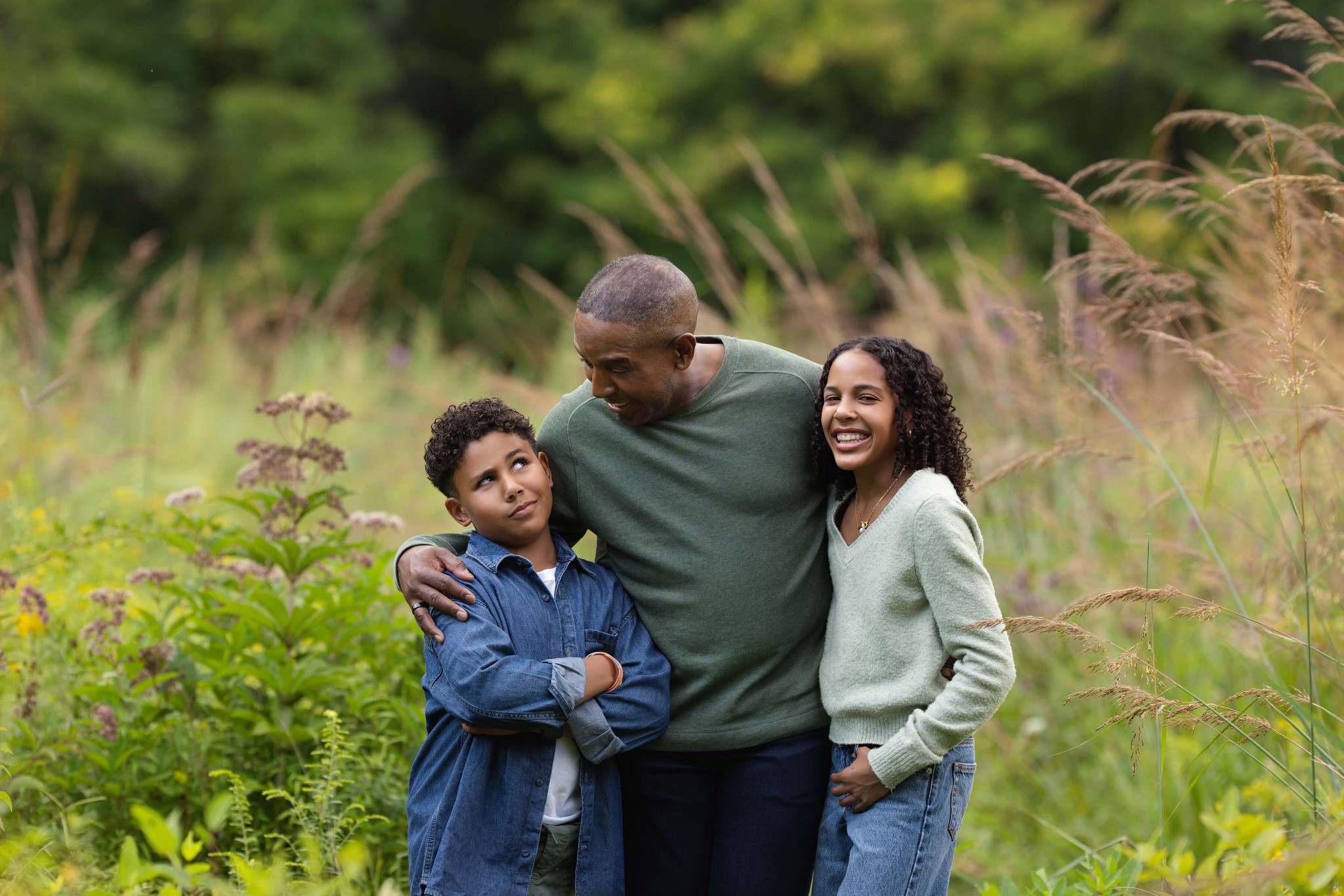 Happy dad embarrasses his son as his daughter laughs in a park lawn after exploring summer camps in summit nj