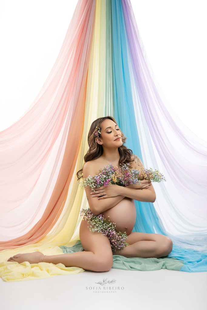 nj maternity photographer captures a mom to be with symbolism of a rainbow baby, draped rainbow fabric and flowers
