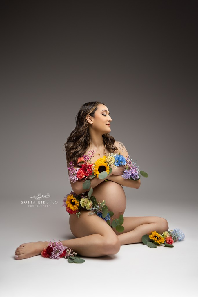 new york maternity photographer captures a mom to be with symbolism of a rainbow baby, with strategically placed rainbow flowers