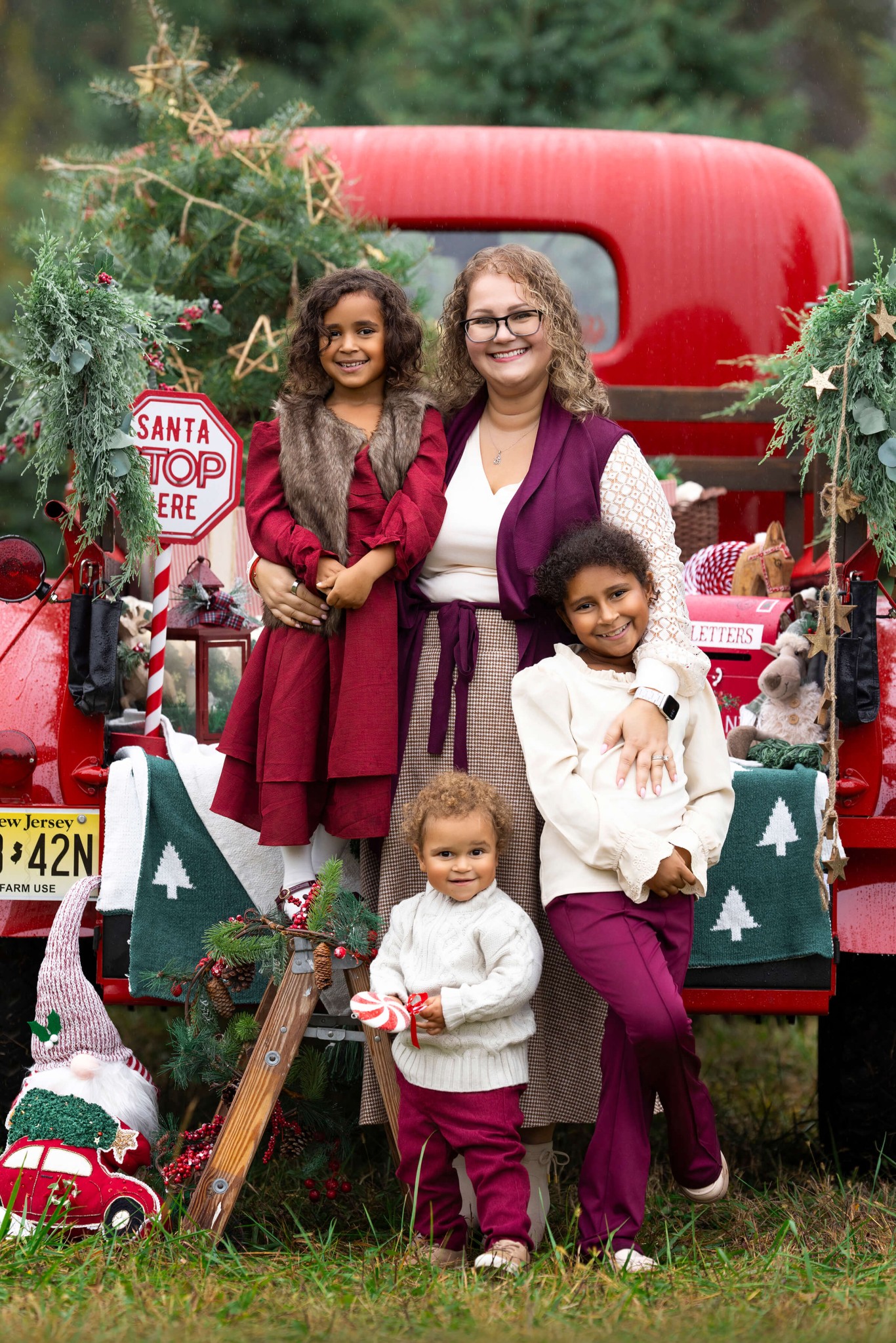 A happy mom stands with arms around her two young duaghters and toddler standing in front of her