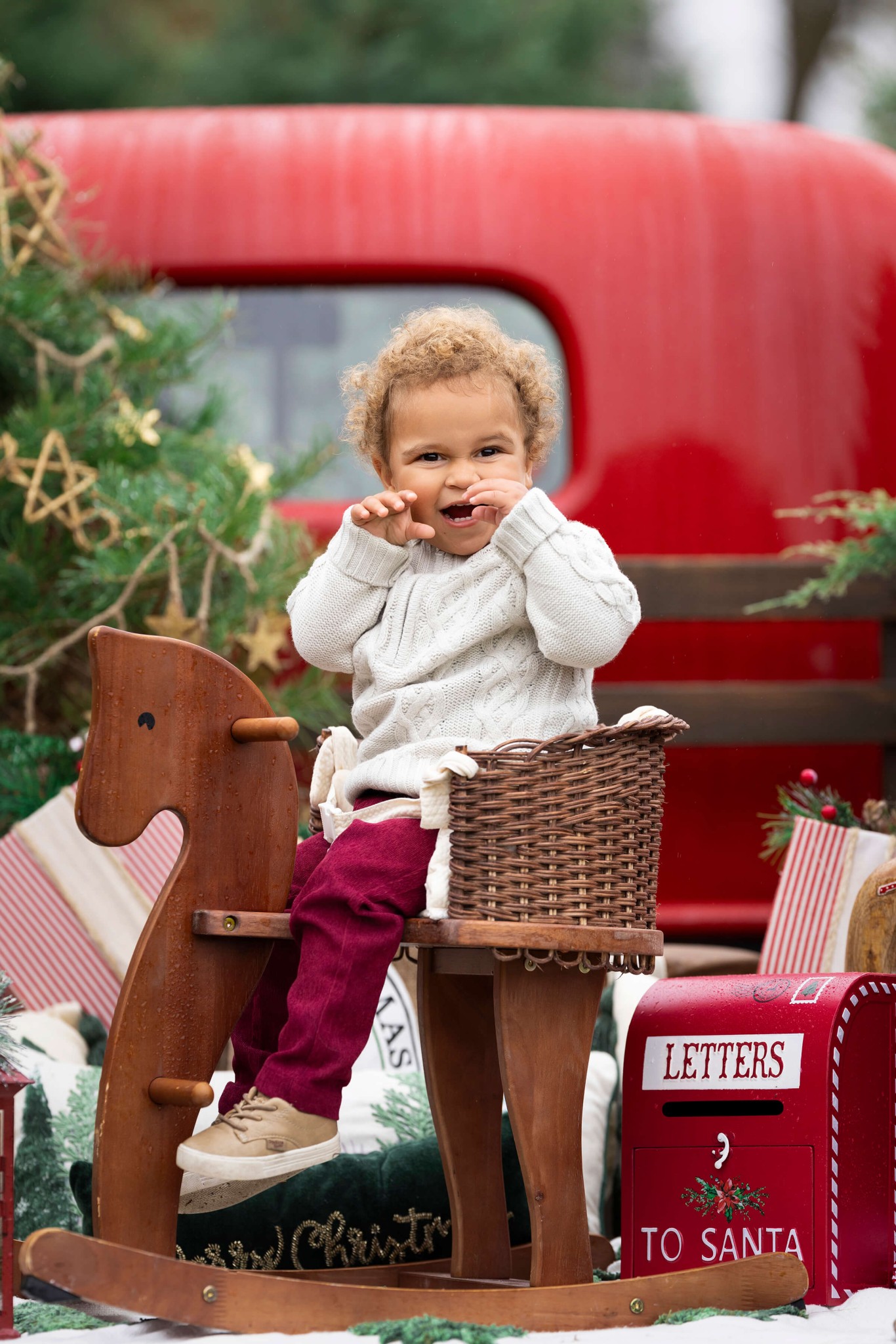 A toddler girl plays on a wooden rocking horse in a white sweater on the back of Santa's truck after visiting daycares in warren nj
