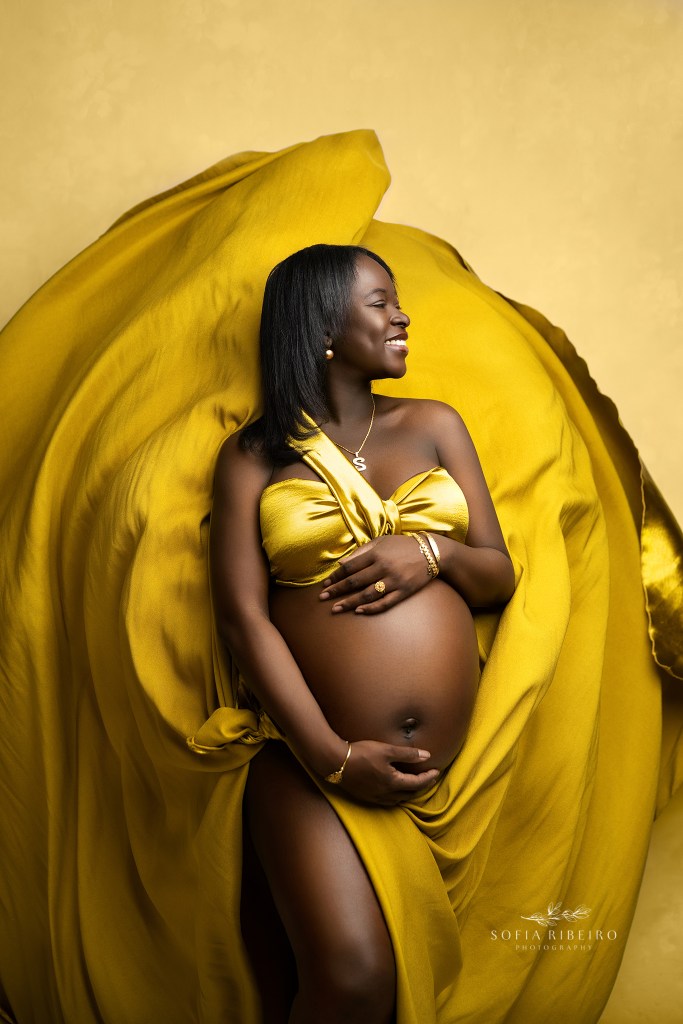 a glowing mom cradled in flowing golden fabric draped against her baby bump