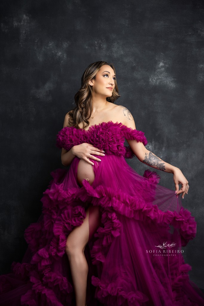 mom poses with hands gently on belly with a hot pink ruffled gown