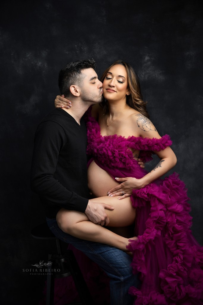 nj maternity photographer captures a mom to be and dad in a sweet moment in a dramatic bold pink and black setup