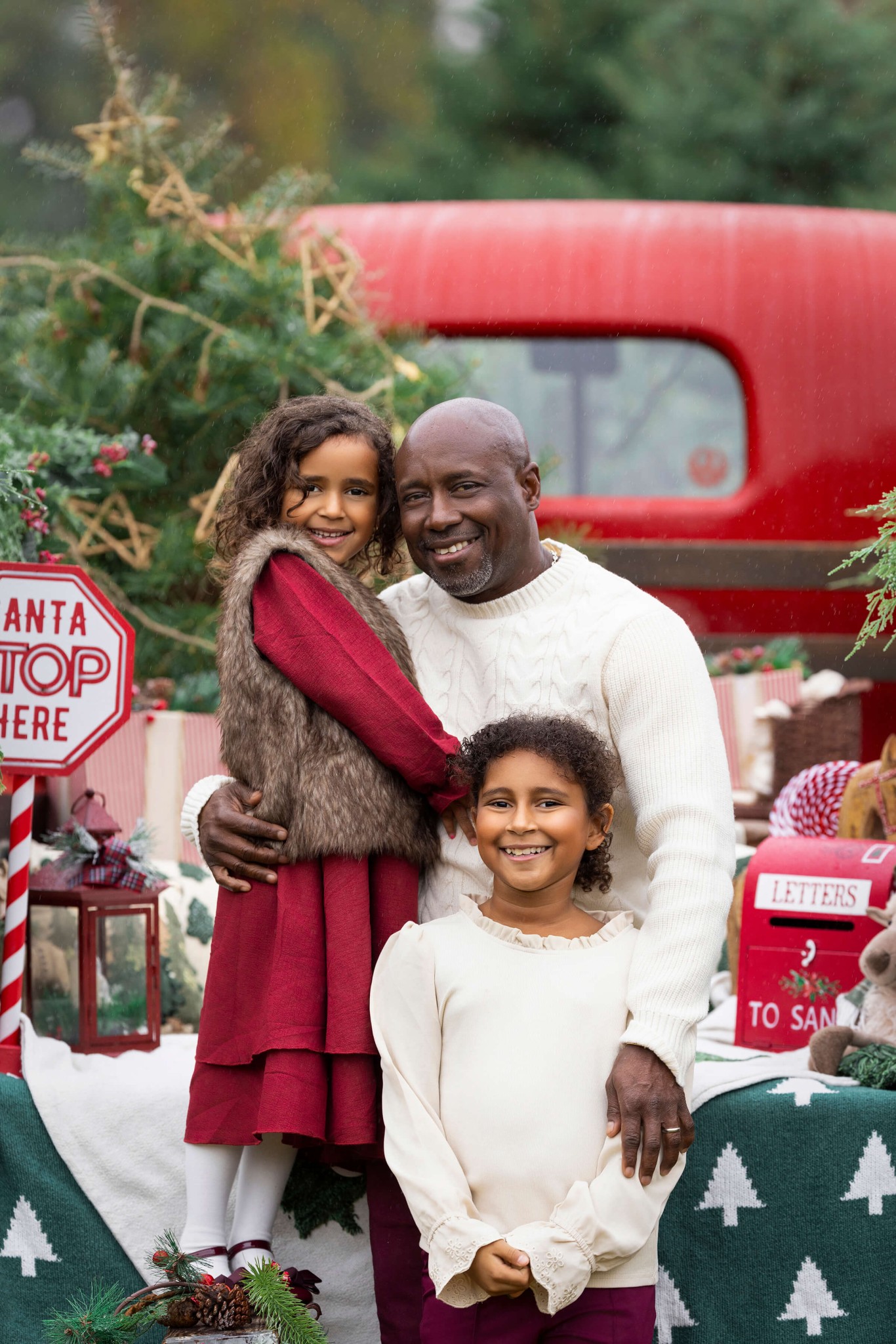 A happy dad hugs his two young daughters in a christmas tree farm